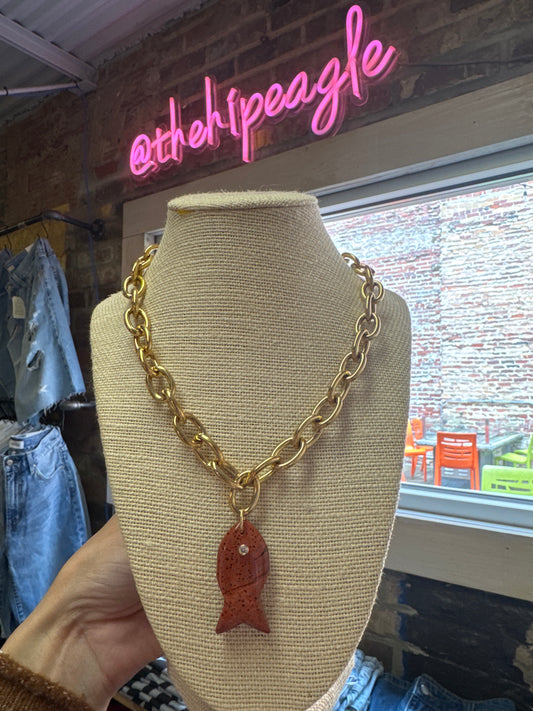 Gold chunky chain necklace with red speckled fish pendant on linen bust