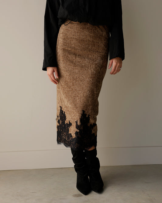 woman wearing a maude brown textured midi skirt with black floral lace trim along the hem, styled with a black blouse and slouchy black boots.