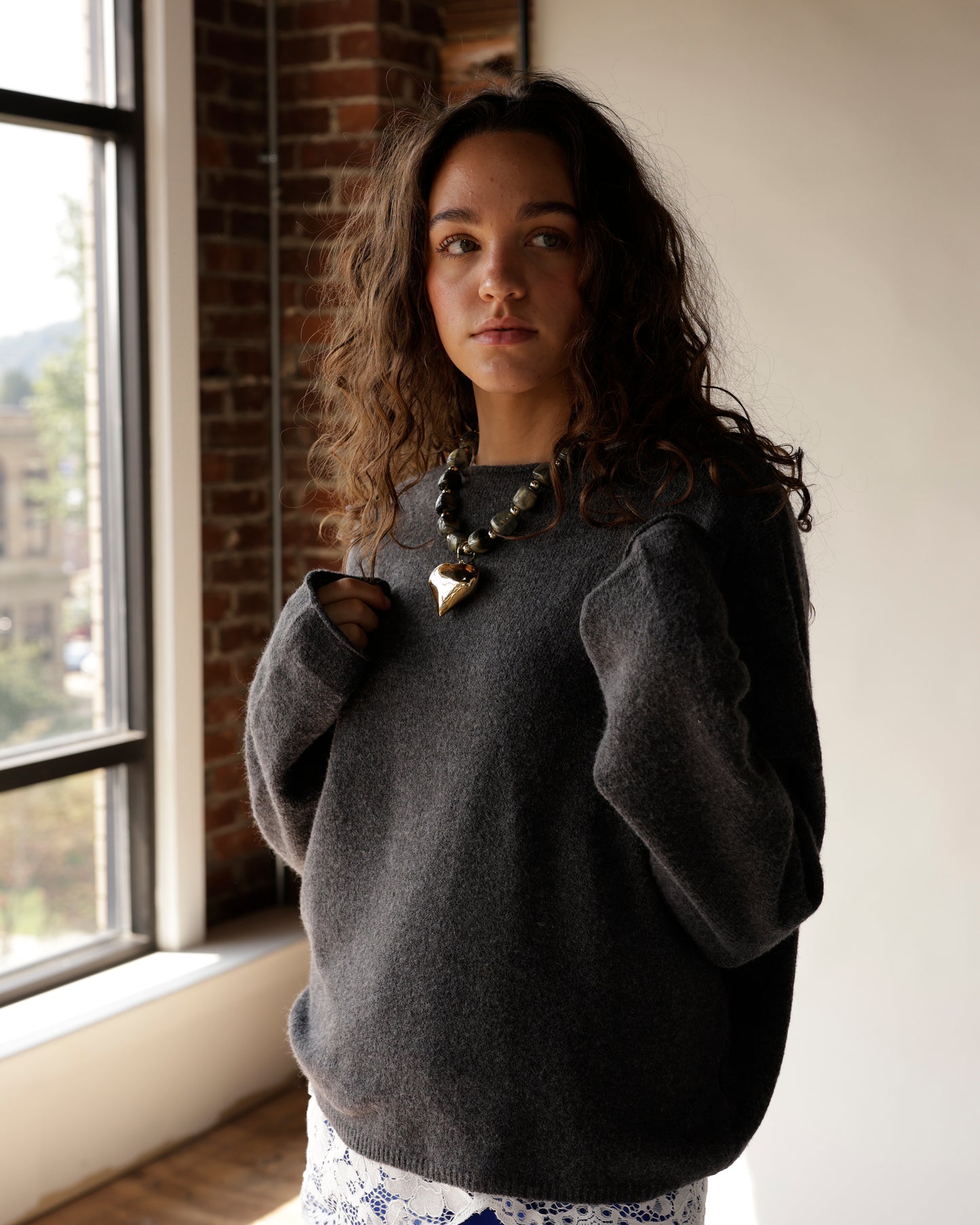 Chunky dark beaded necklace with gold heart pendant worn over gray sweater