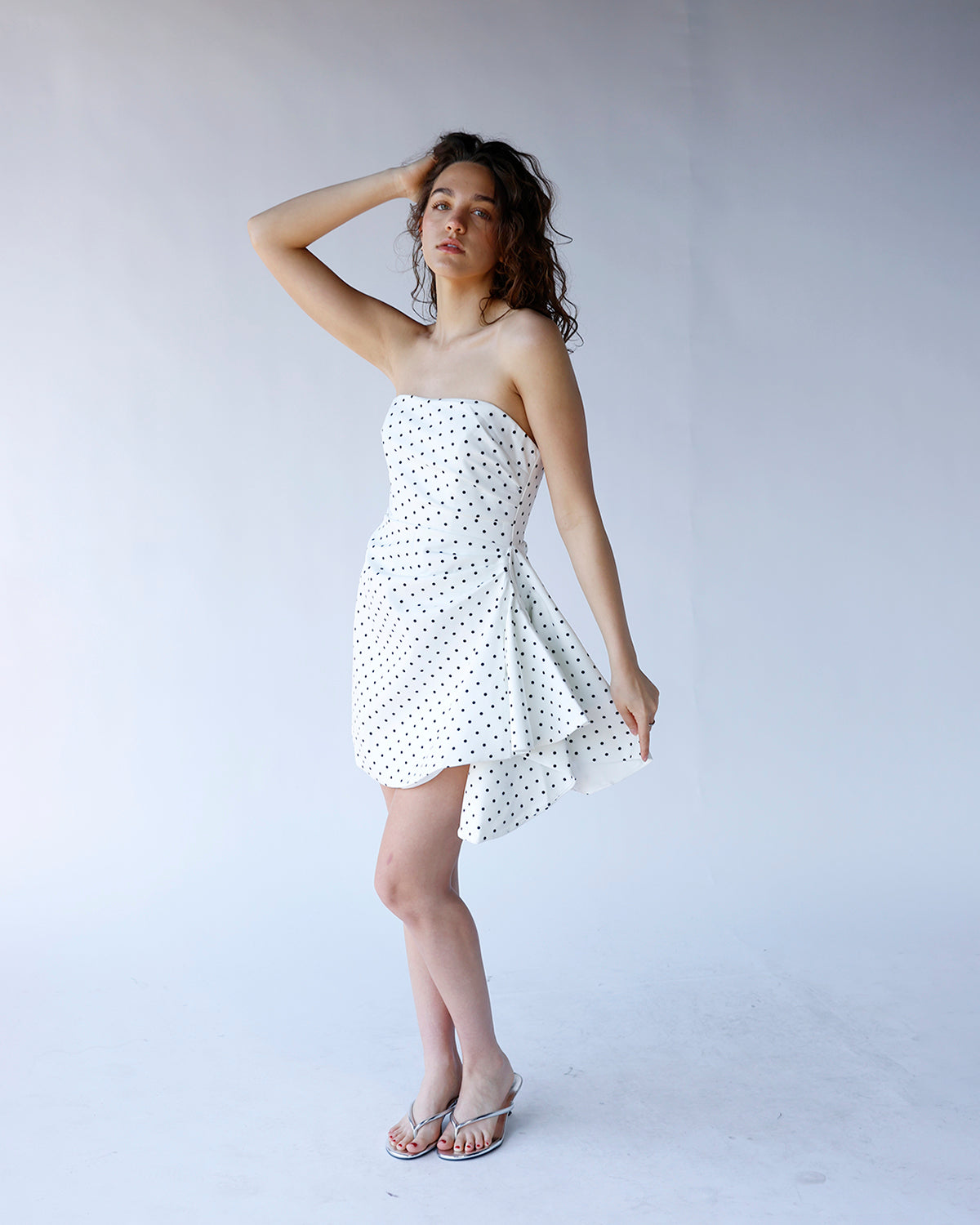 White strapless mini dress with black polka dots and flared skirt, styled with silver sandals.
