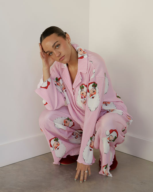 pink and white pinstripe christmas pajama set featuring oversized vintage santa face prints, a notched collar, button-front top and matching wide-leg pants.