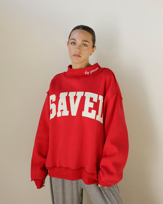 shop the bucketlist saved by grace sweatshirt in bold red with cream varsity lettering, mock neckline and an oversized fit. faith-inspired style with attitude.