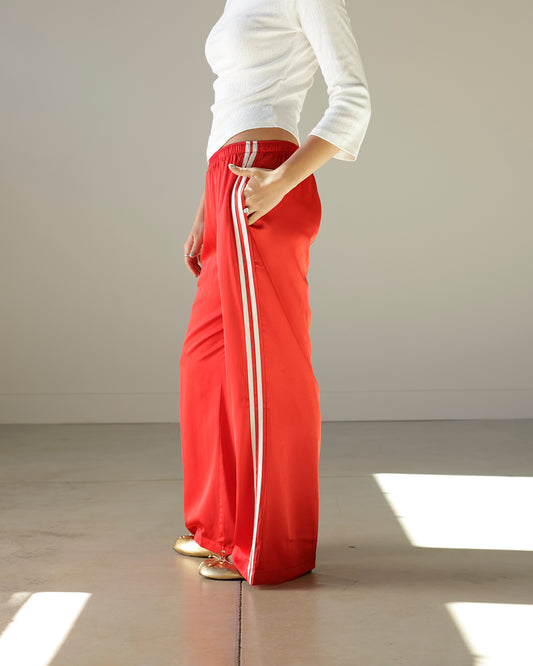 Loucia cherry red satin-look track pants featuring contrasting ivory side stripes, an elastic waistband, side pockets and a relaxed wide-leg silhouette.