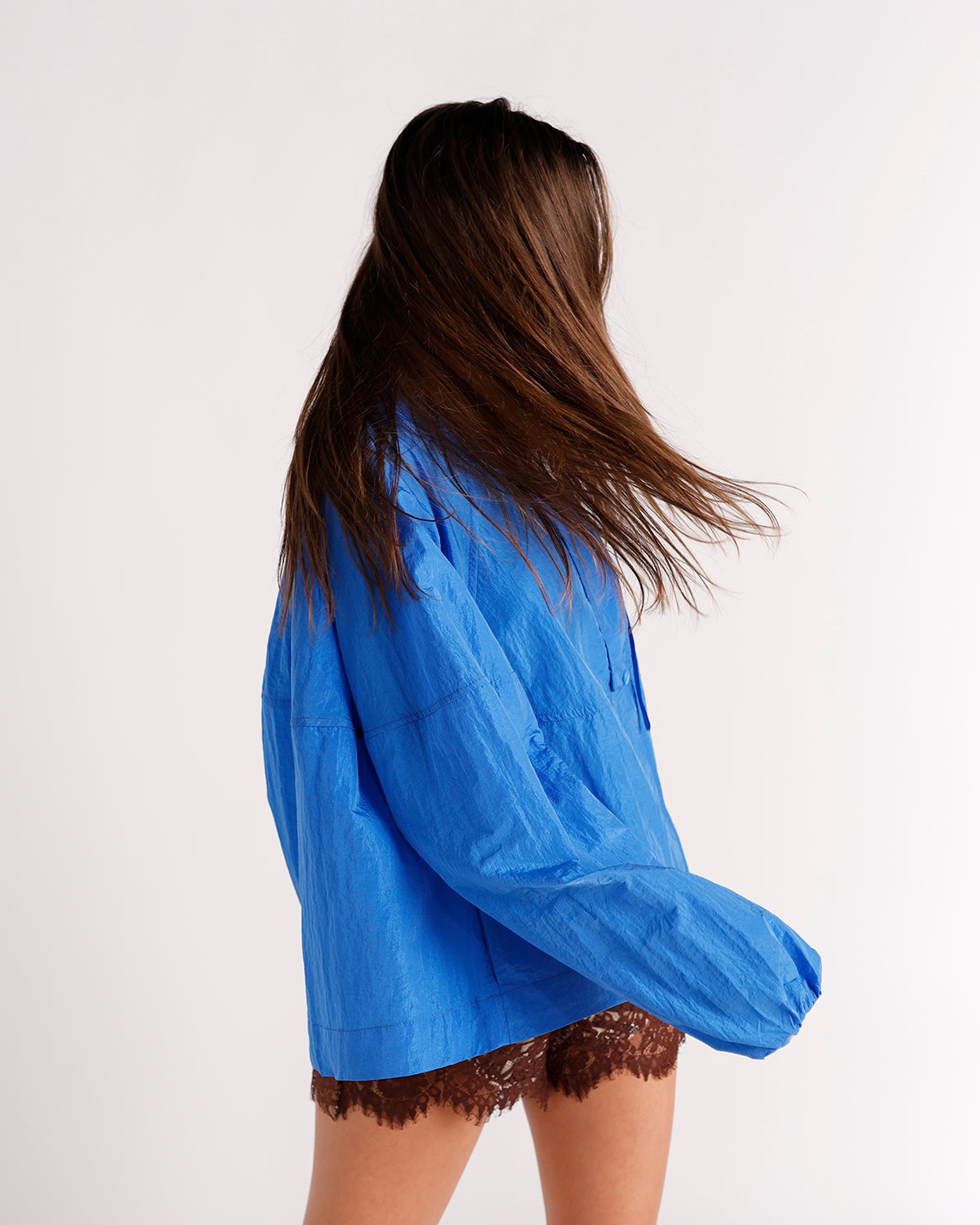 Bright blue oversized windbreaker jacket with balloon sleeves, worn over brown lace shorts.