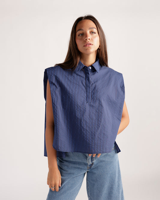 Fashionable navy blue, striped sleeveless top with a unique, architectural design. Features open sides, a pointed collar, and a single button.