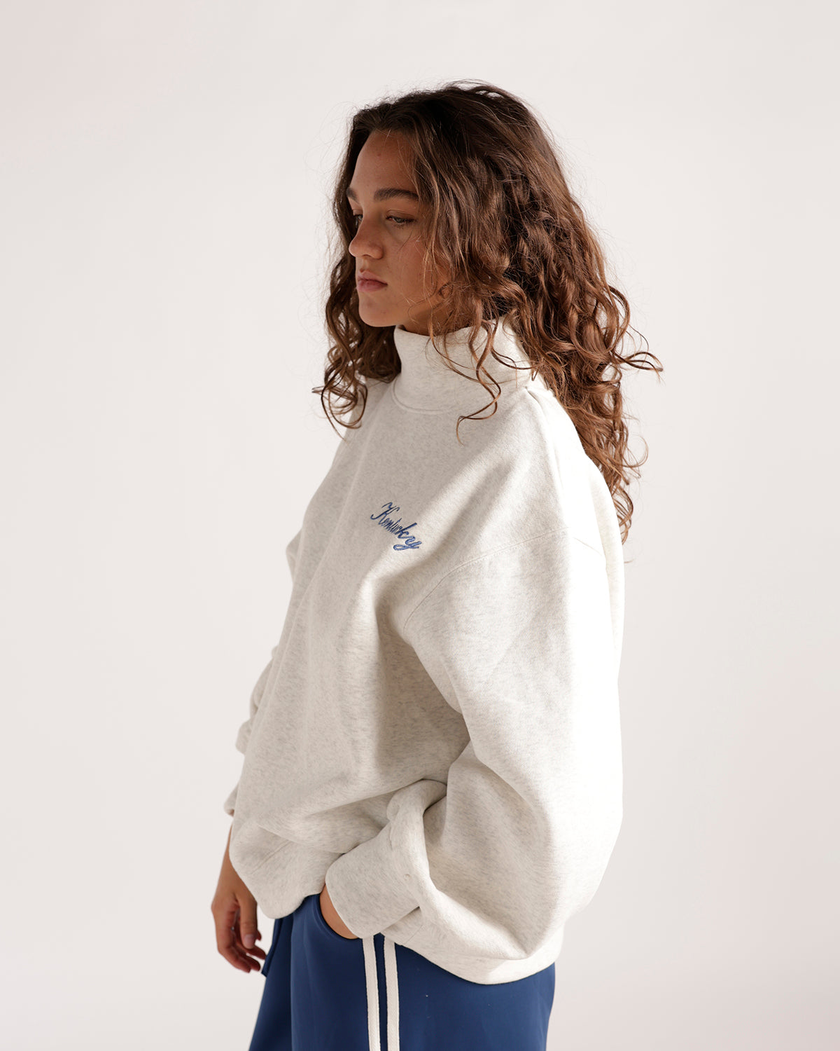 Oversized cream mock neck sweatshirt with blue script lettering, paired with blue track pants
