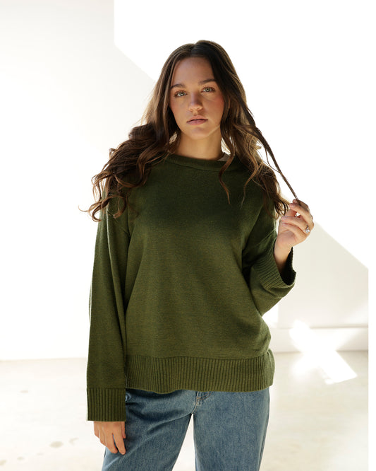 model wearing a green sweater and jeans holding her hair