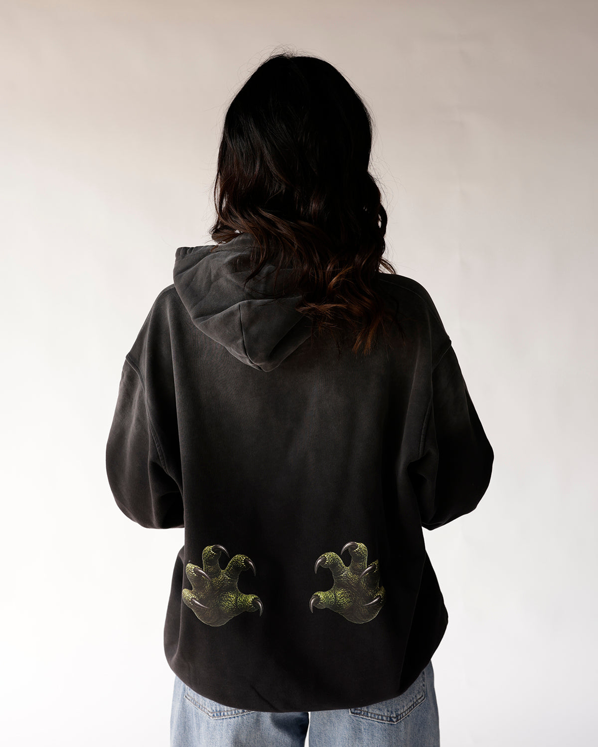 Back view of black oversized hoodie with green dinosaur claws graphic print