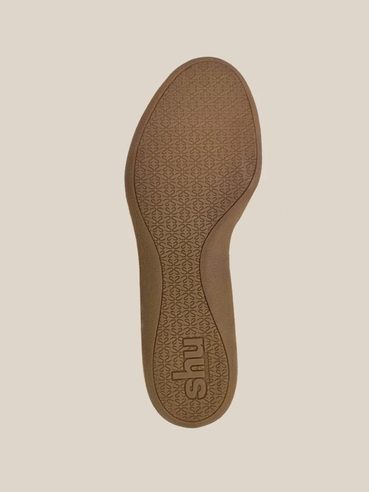 Bottom sole of a tan flat sneaker with textured floral grip pattern