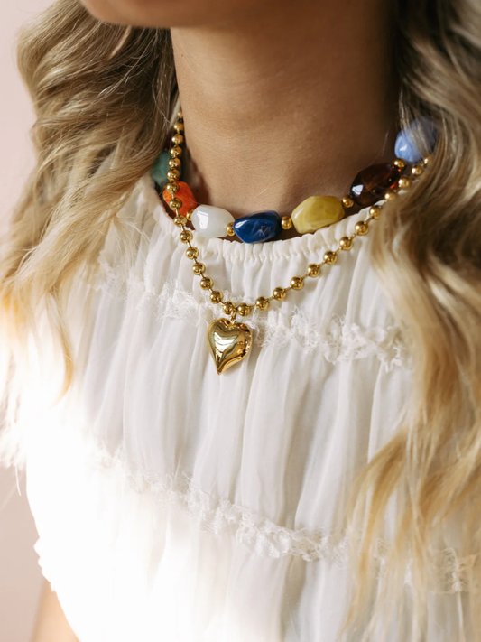 Gold beaded necklace with colorful stones and heart pendant on white top