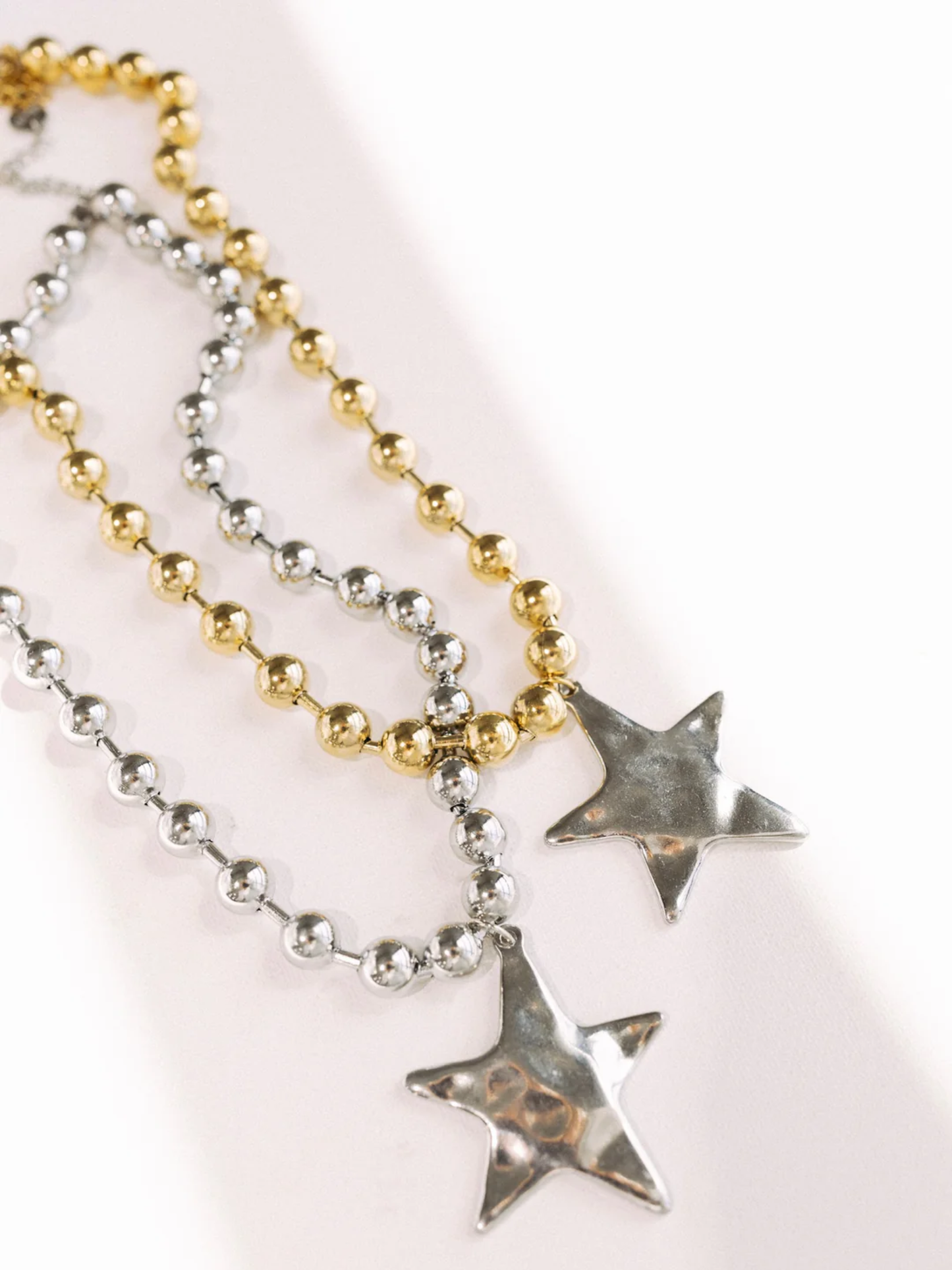 Silver and gold ball chain necklaces with silver star pendants on white background