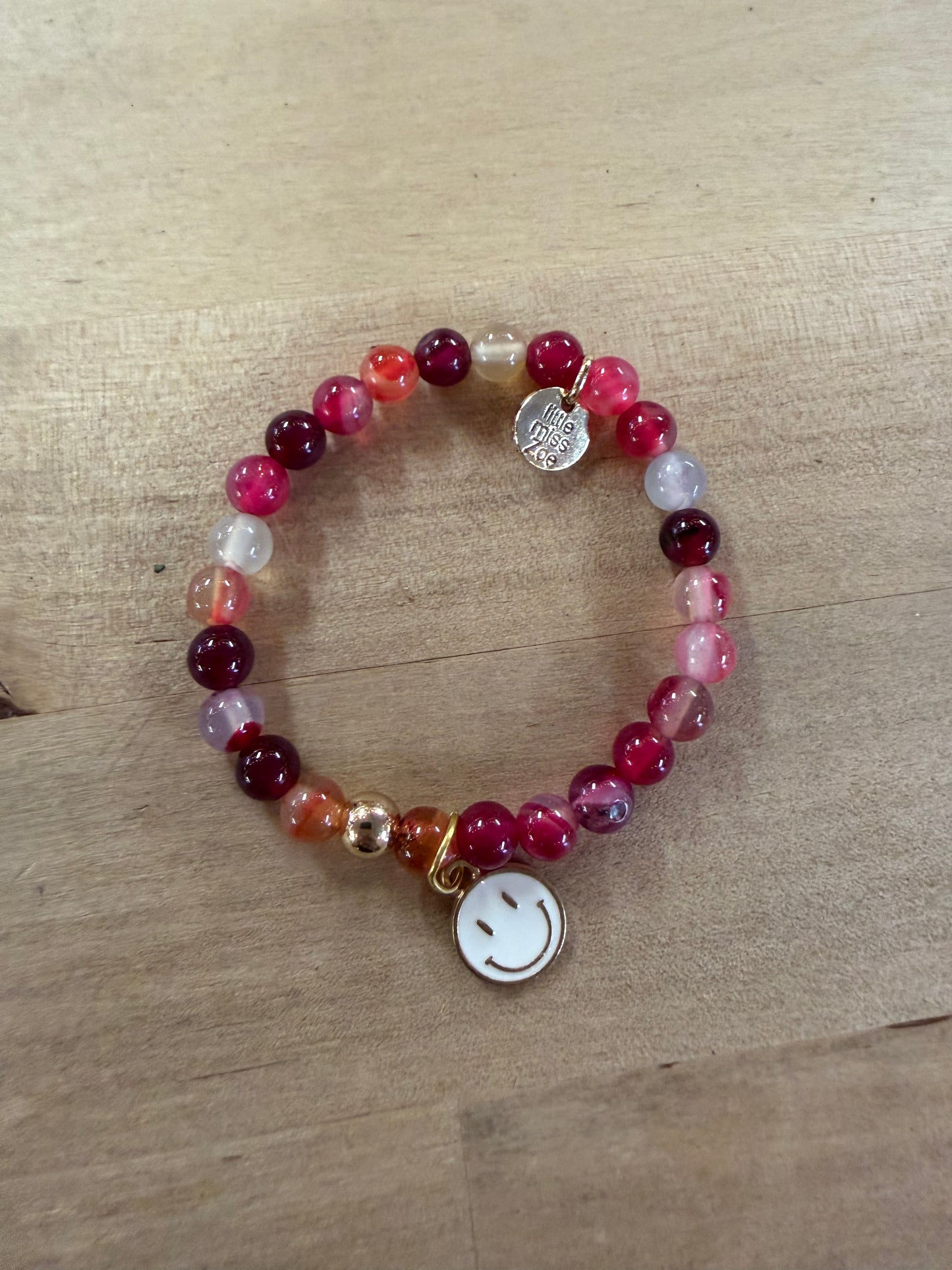 Beaded stretch bracelet in pink and red tones with smiley face charm