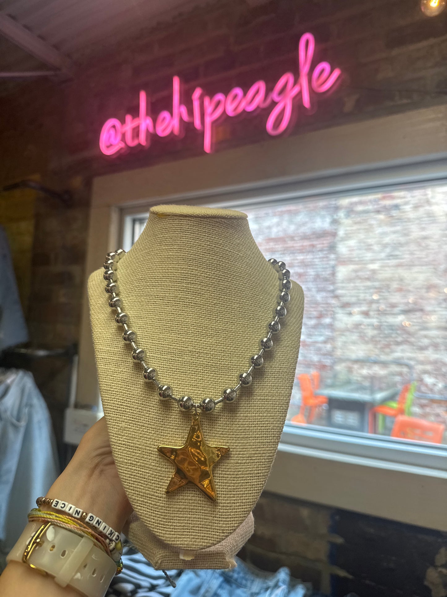 Silver beaded necklace with hammered gold star pendant on linen jewelry bust