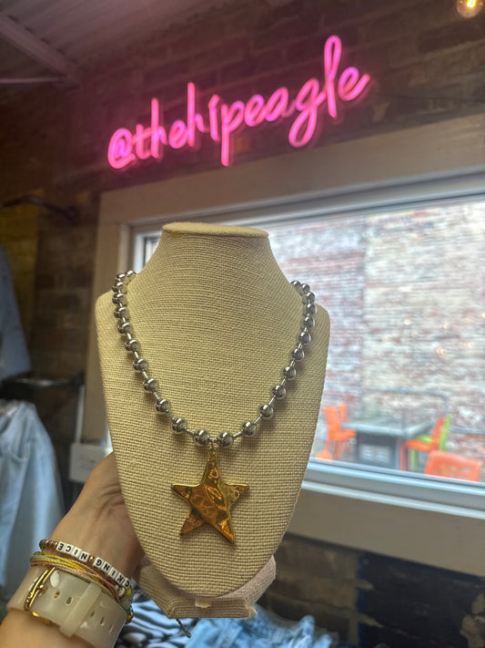 Silver beaded necklace with hammered gold star pendant on linen jewelry bust