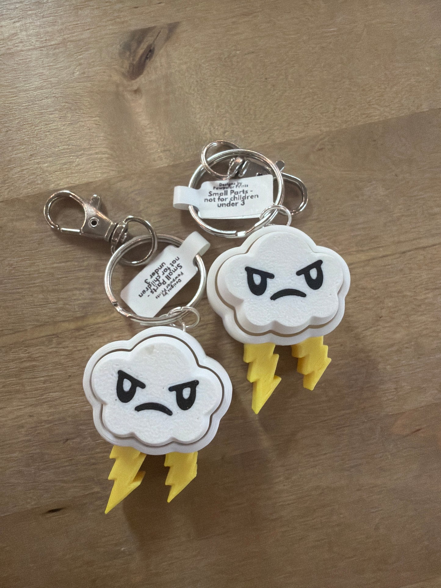 Two white angry storm cloud keychains with yellow lightning bolts on wood surface