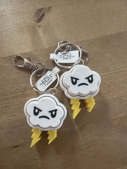 Two white angry storm cloud keychains with yellow lightning bolts on wood surface