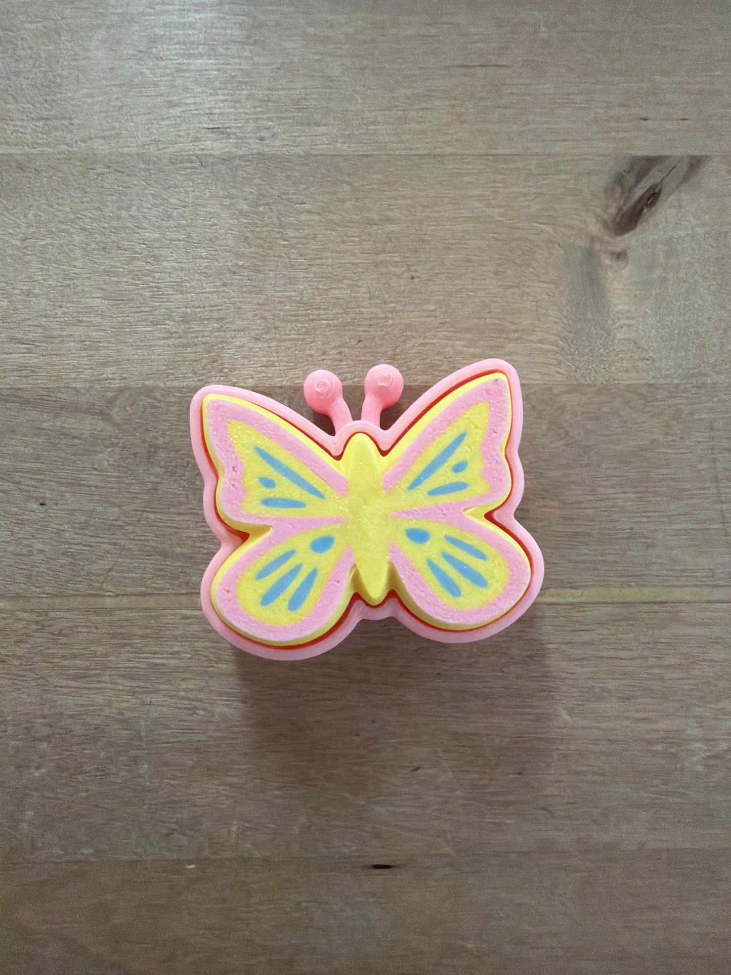 Pink and yellow butterfly-shaped clicker toy with blue wing details and antennae