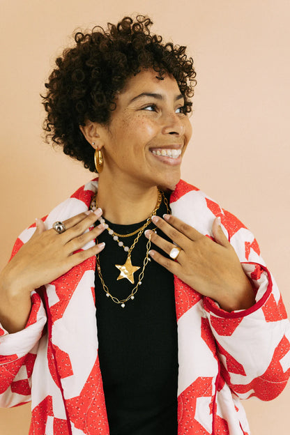 Gold star pendant layered chain necklace with pearl accents worn by smiling woman