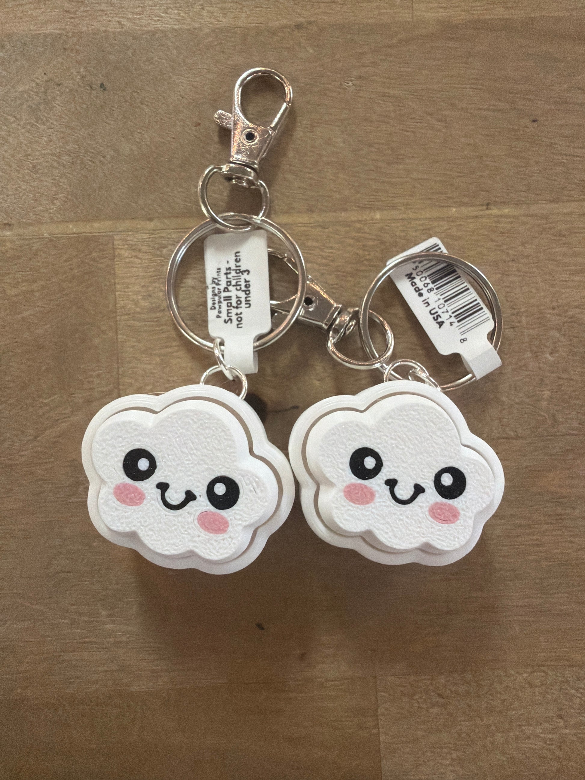 Two white kawaii cloud-shaped clicker keychains with smiley faces, silver hardware
