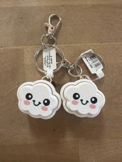 Two white kawaii cloud-shaped clicker keychains with smiley faces, silver hardware