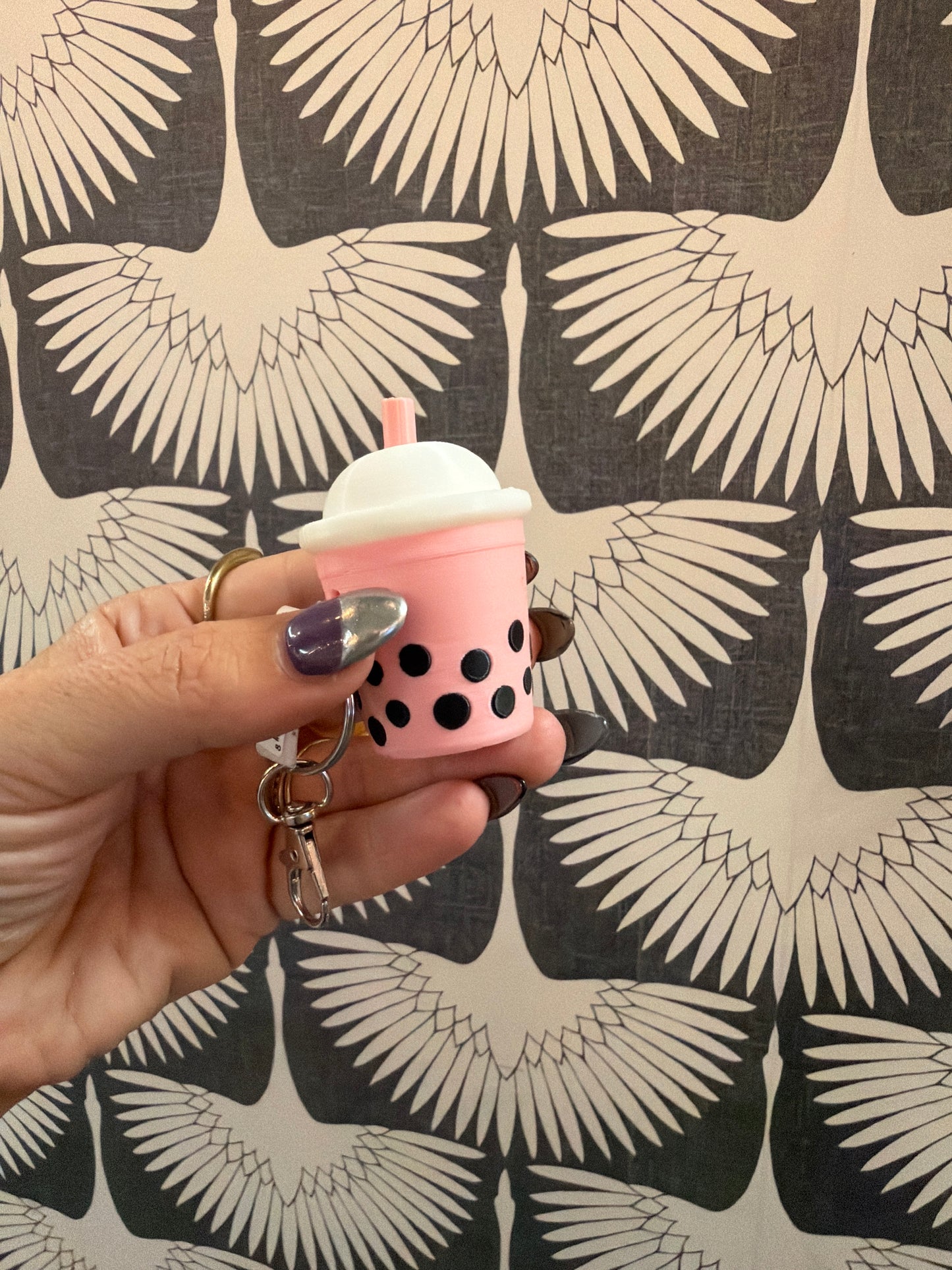 Pink boba tea bubble tea keychain clicker held in hand against bird wallpaper