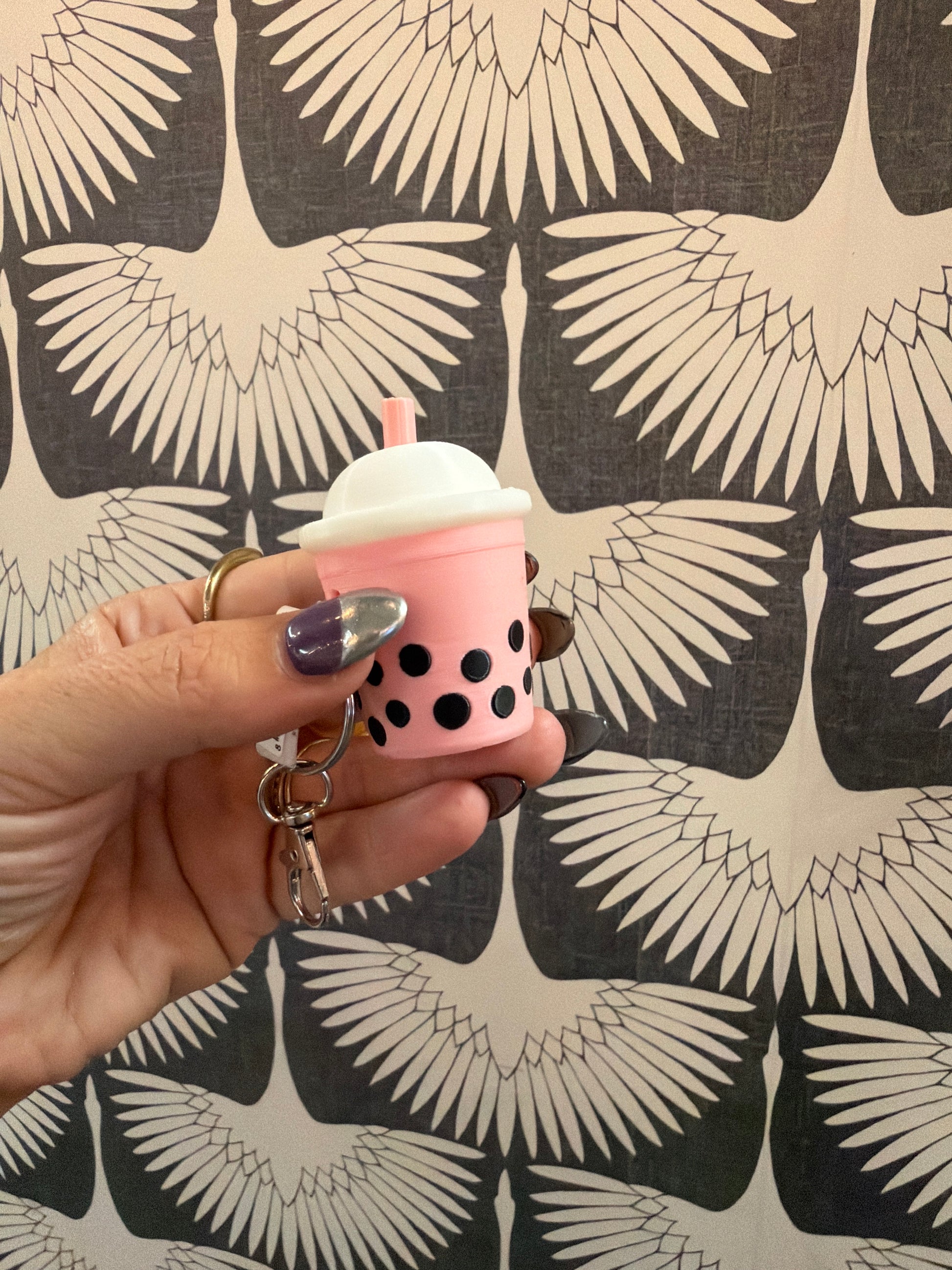 Pink boba tea bubble tea keychain clicker held in hand against bird wallpaper