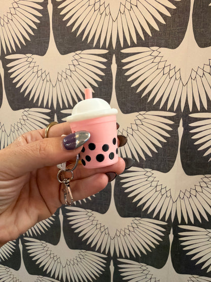 Pink boba tea bubble tea keychain clicker held in hand against bird wallpaper