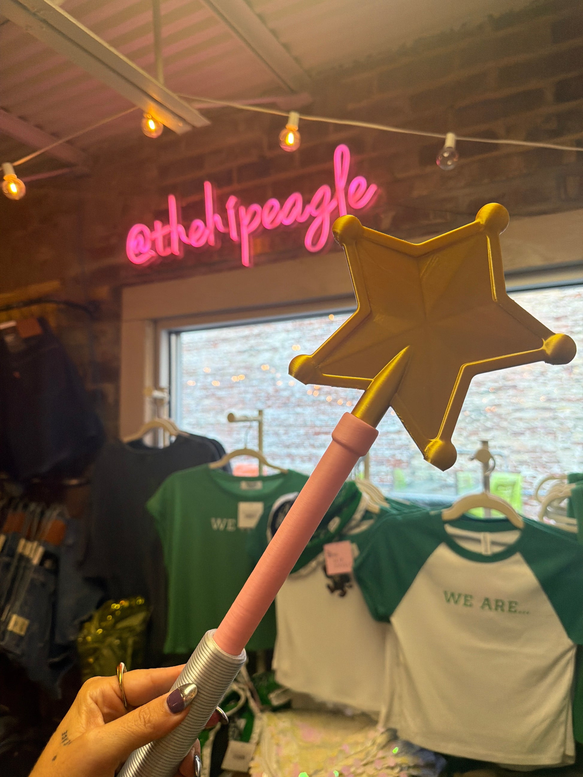 Gold star magic wand with pink handle held up in boutique store