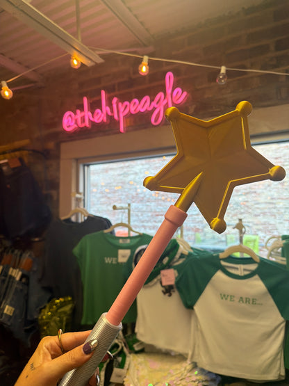 Gold star magic wand with pink handle held up in boutique store