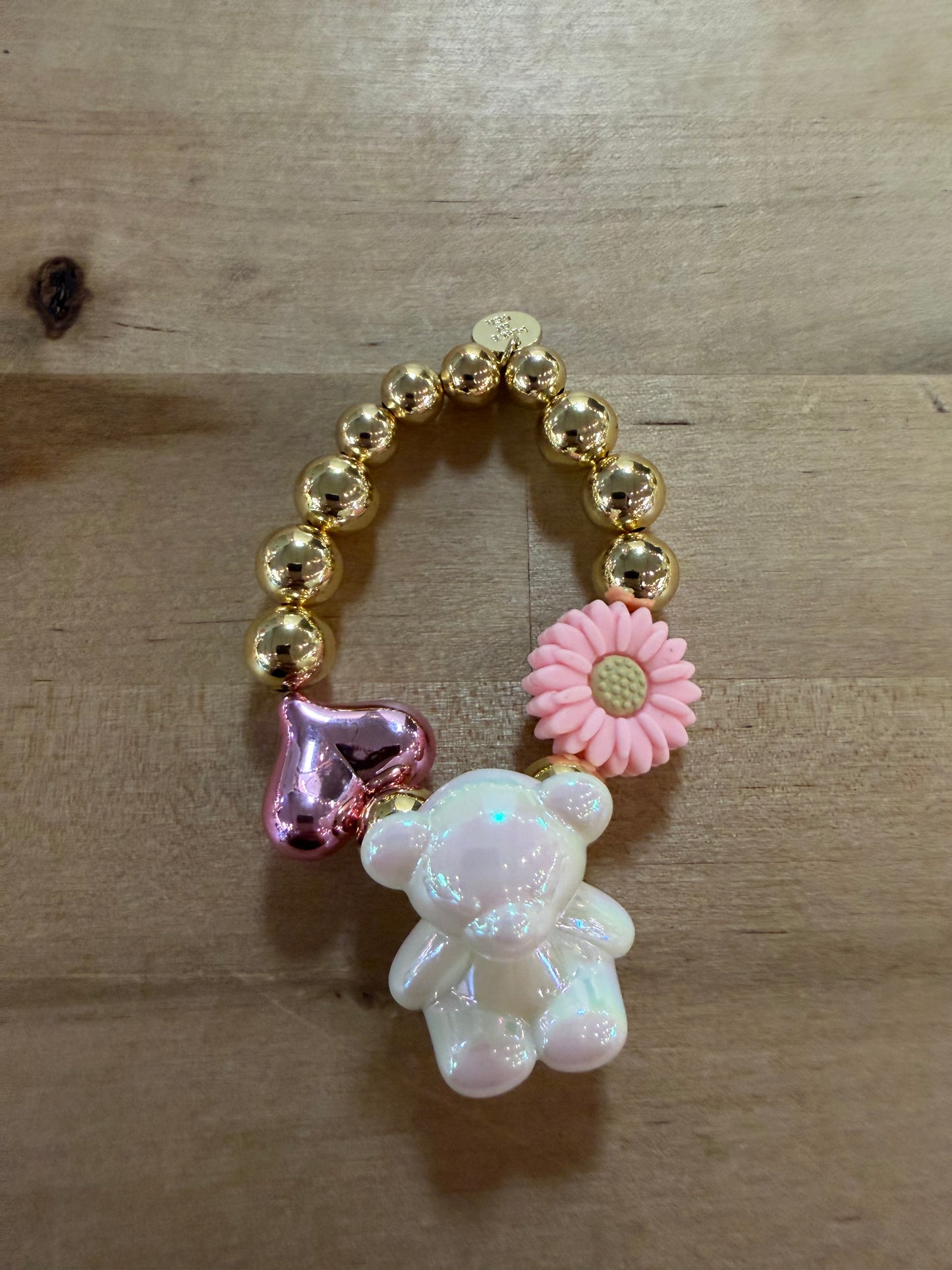 Gold beaded bracelet with pearlescent bear, pink flower, and metallic heart charms