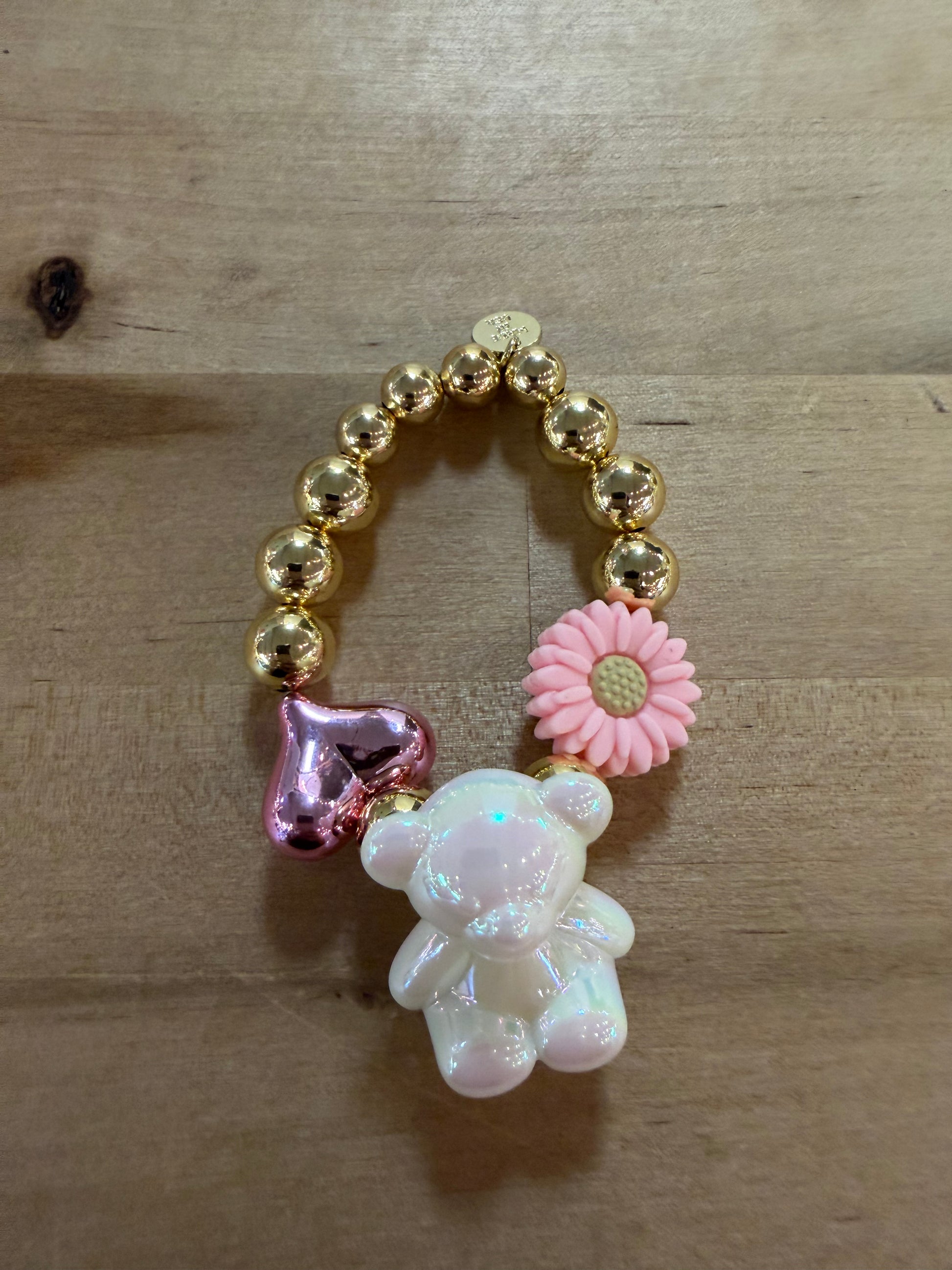 Gold beaded bracelet with pearlescent bear, pink flower, and metallic heart charms