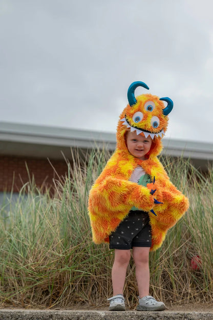Child wearing orange fuzzy monster cape with blue horns, teeth, and googly eyes