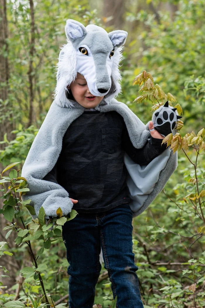 Child wearing gray wolf costume cape with hood and paw gloves in forest