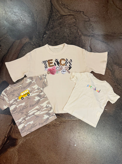 Three kids tees: camo with school bus, cream TEACH graphic, cream pre-skool print