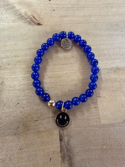 Blue beaded stretch bracelet with black enamel smiley face charm and silver accents.