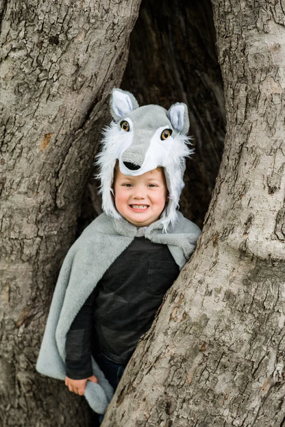 Child wearing gray wolf cape costume with hooded wolf face, posed in tree hollow