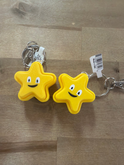Two yellow star-shaped smiley face clicker keychains on a wood surface