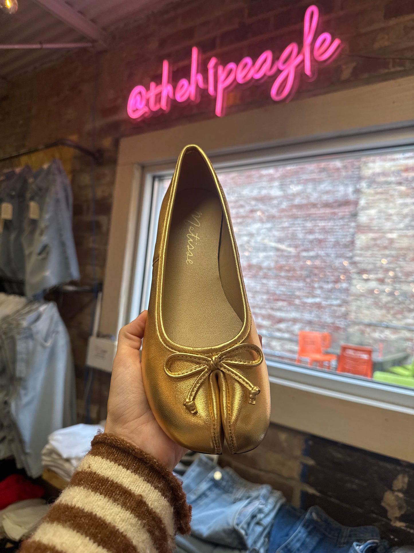 Gold metallic split-toe ballet flat with bow detail, held up in boutique