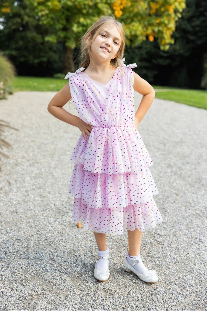 Girl wearing pink tiered ruffle dress with colorful sprinkle print and bow shoulders