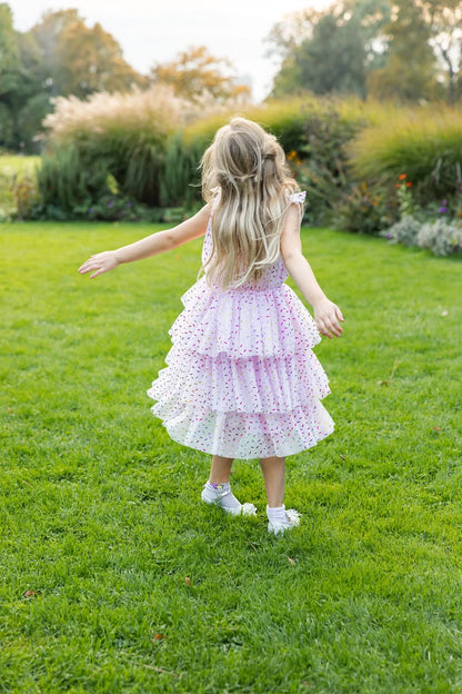Girl twirling in pink tiered ruffle dress with colorful sprinkle print, outdoors