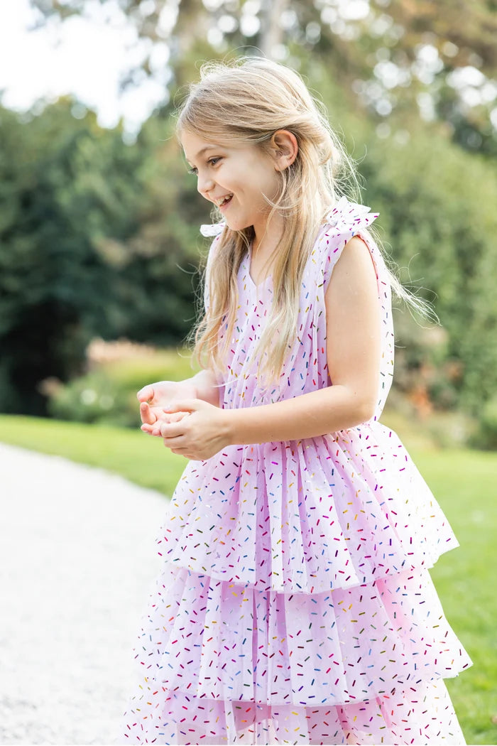 Girl wearing pink tiered ruffle dress with colorful sprinkle print, sleeveless