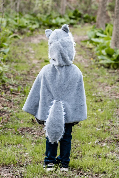 Child wearing gray wolf cape costume with hood, ears, and tail in forest