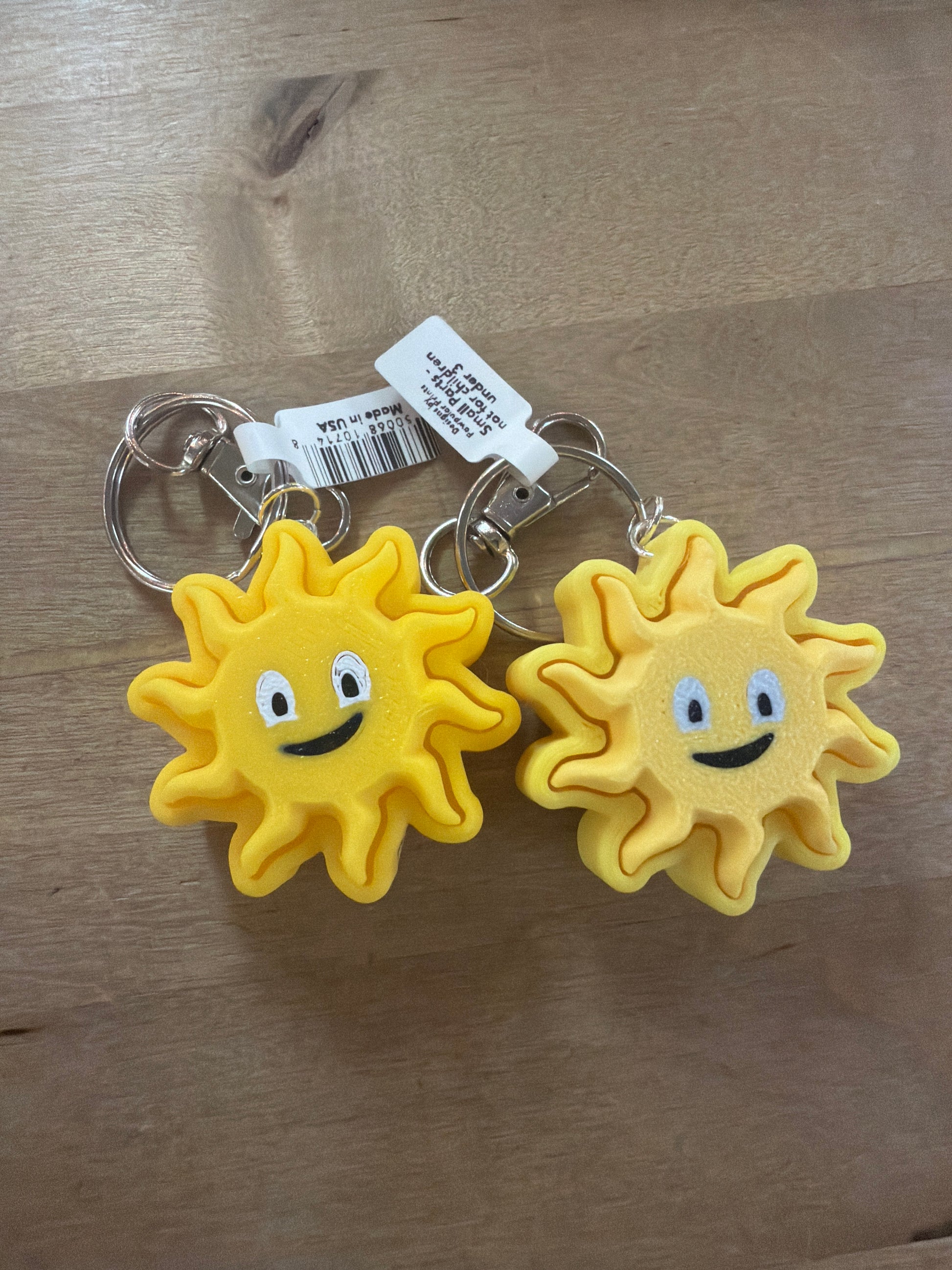 Two yellow smiling sun face rubber keychains with silver key rings on wood surface