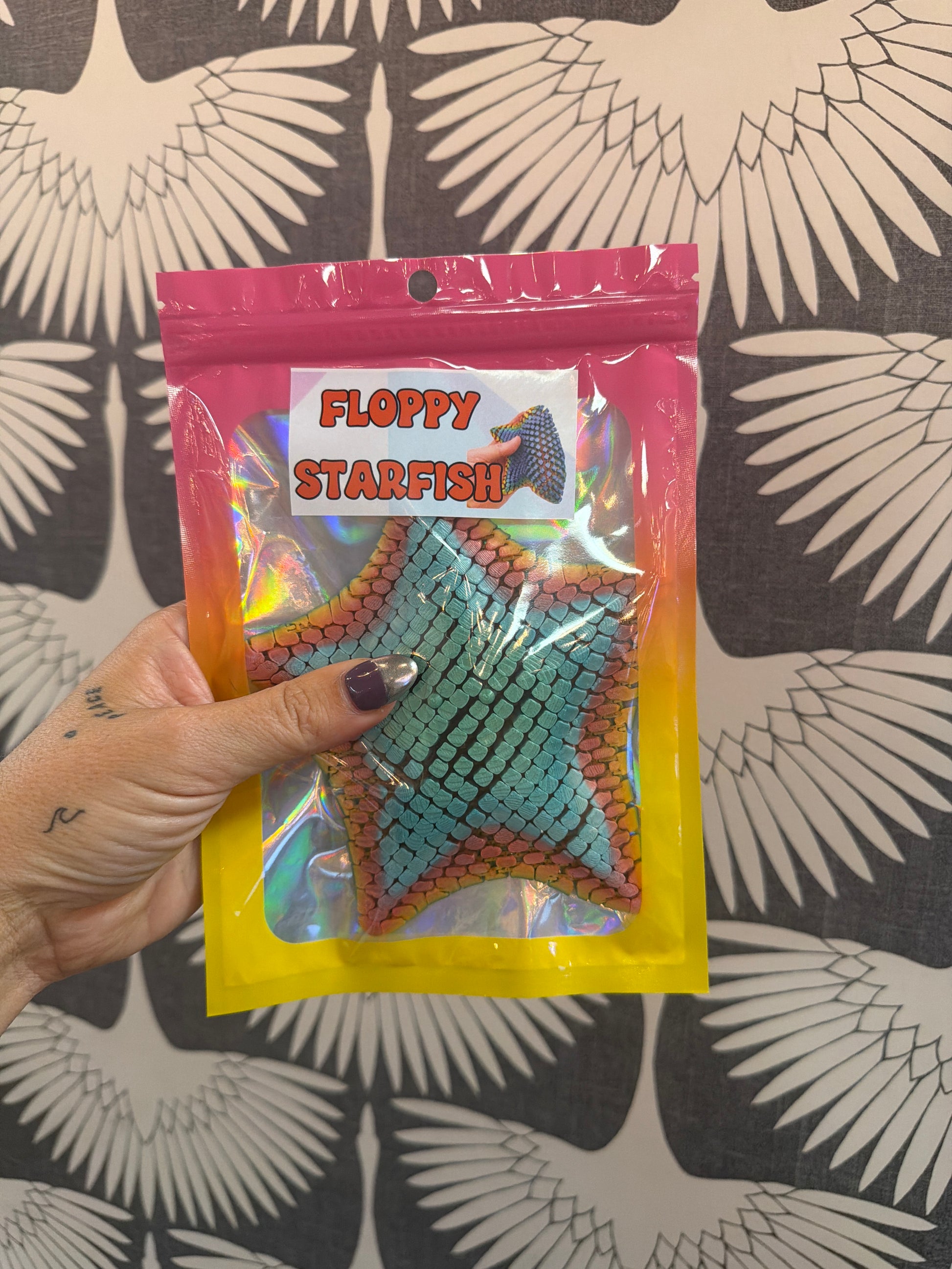 Floppy Starfish fidget toy in teal scale texture, shown in holographic pink-yellow resealable bag
