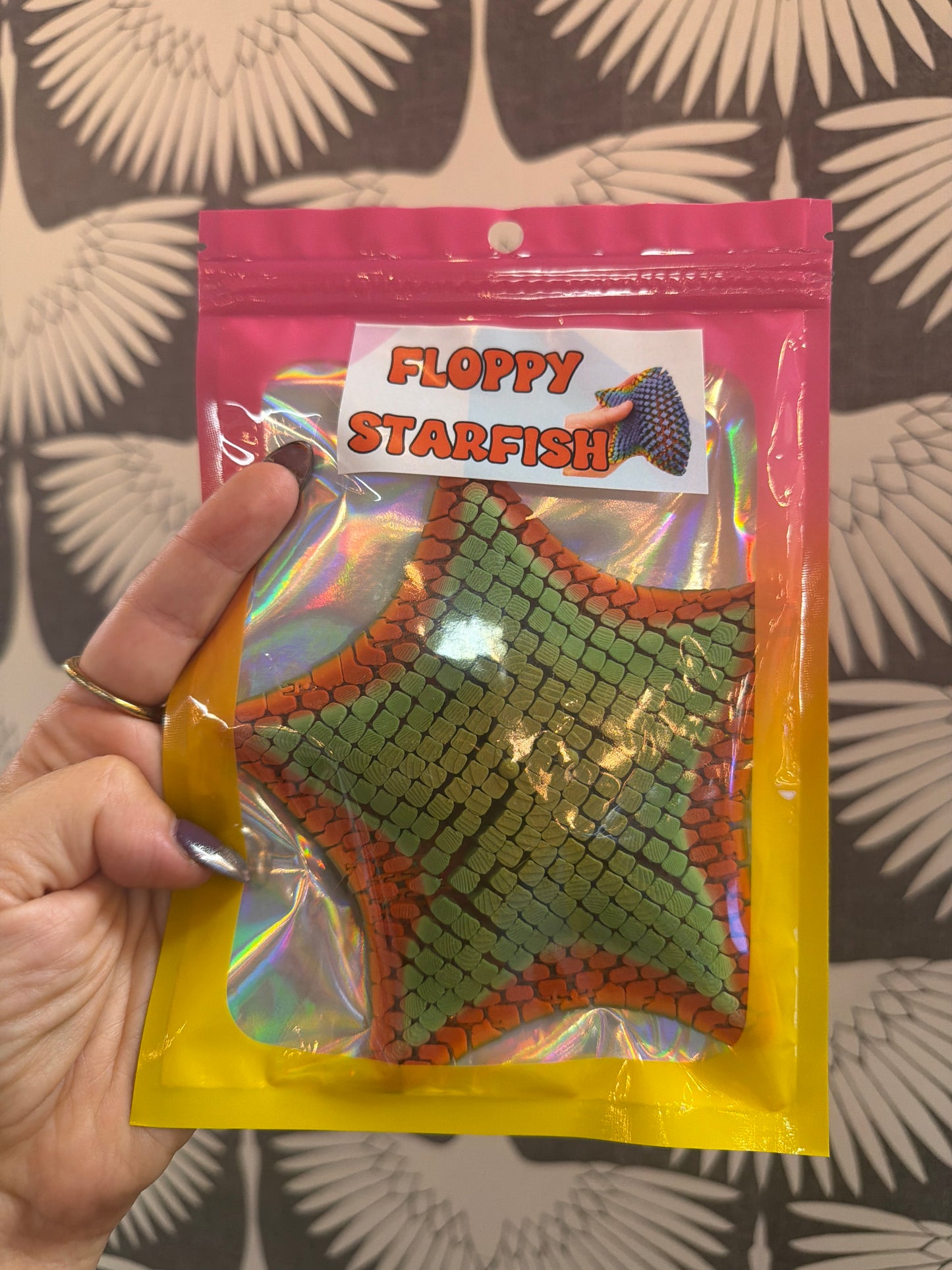 Floppy Starfish fidget toy in green and orange scale texture, holographic packaging