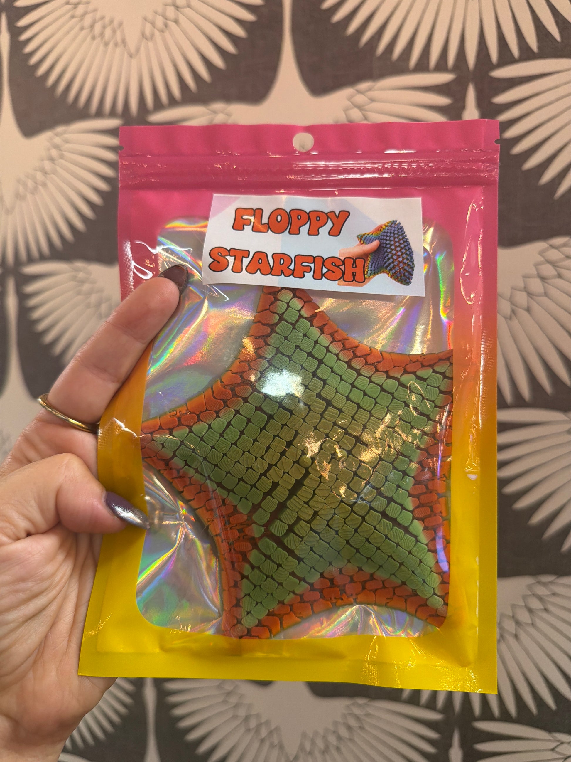 Floppy Starfish fidget toy in green and orange scale texture, holographic packaging