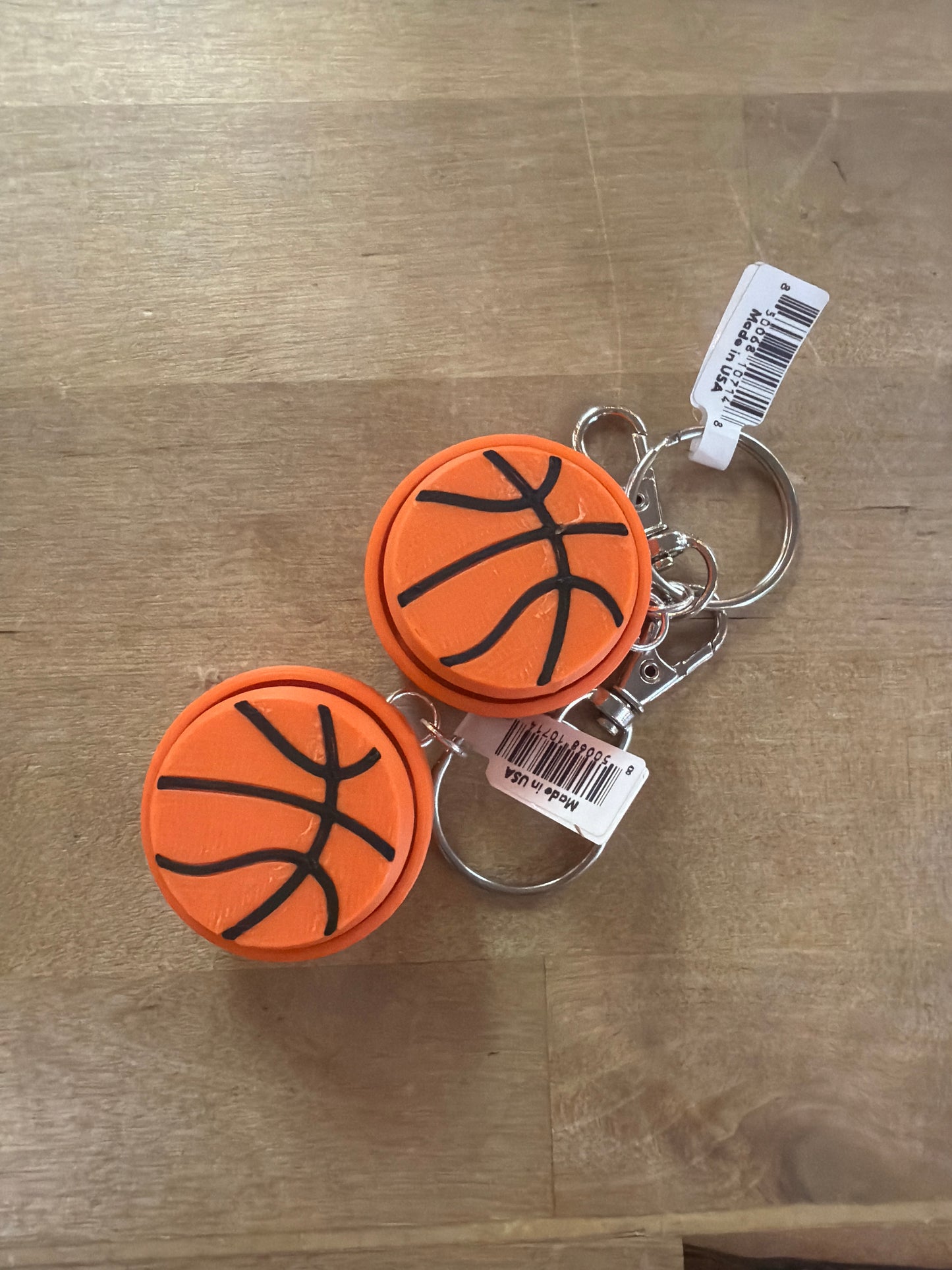 Two orange basketball-shaped clicker keychains with black seam lines, Made in USA