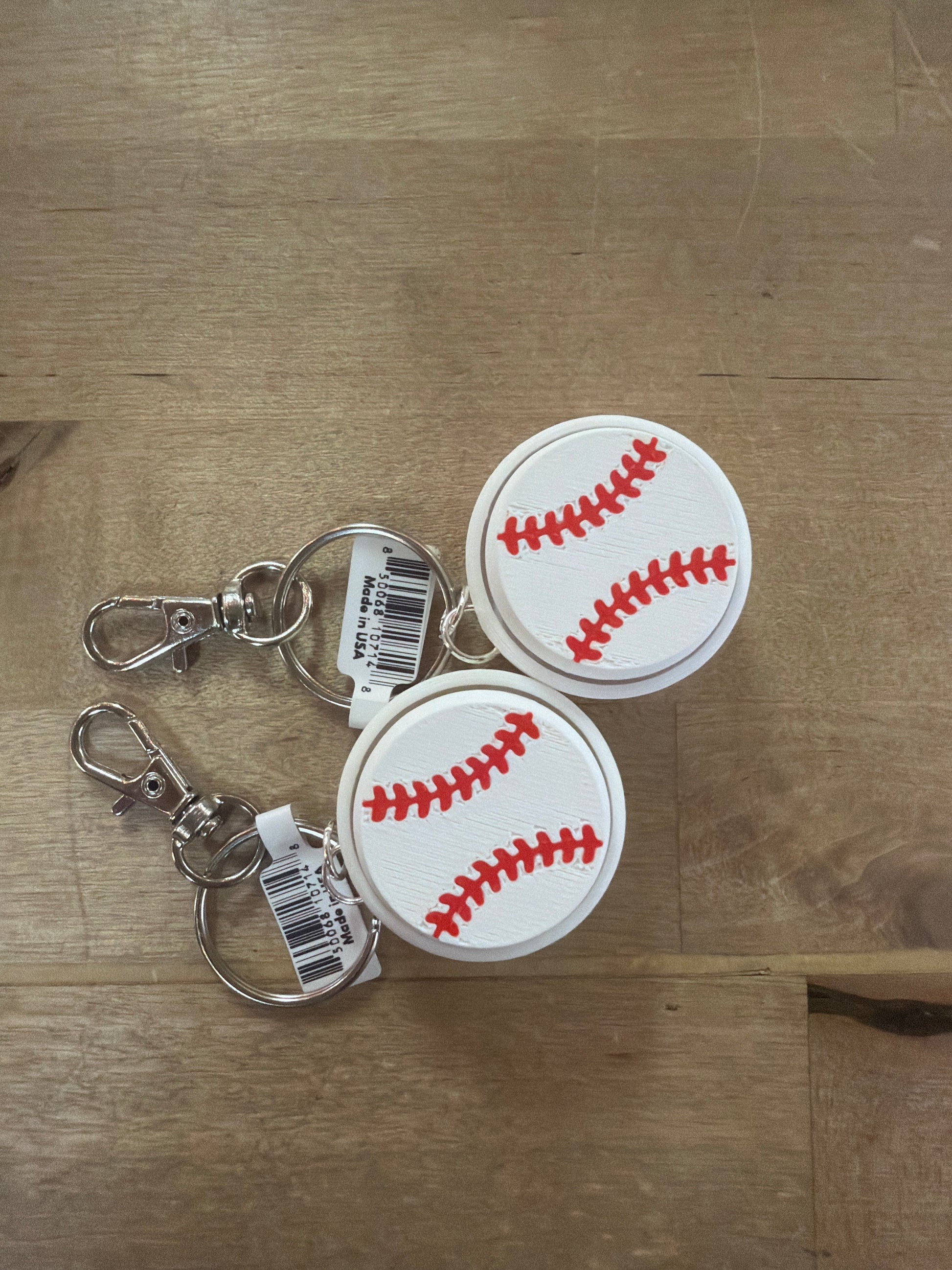 Two baseball-shaped white rubber keychain clickers with red stitching detail, silver clasp