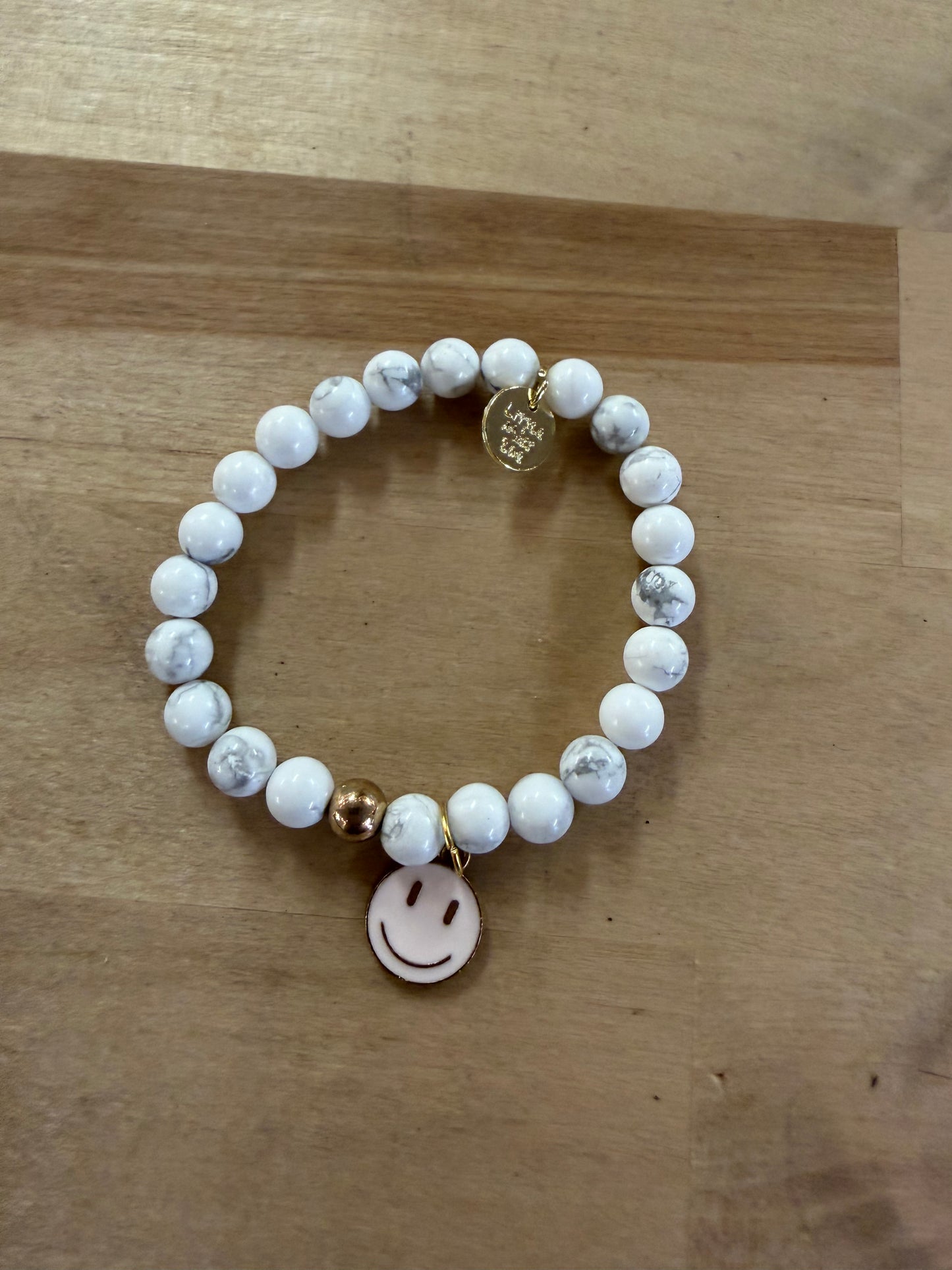 White marble beaded stretch bracelet with gold smiley face charm and logo tag