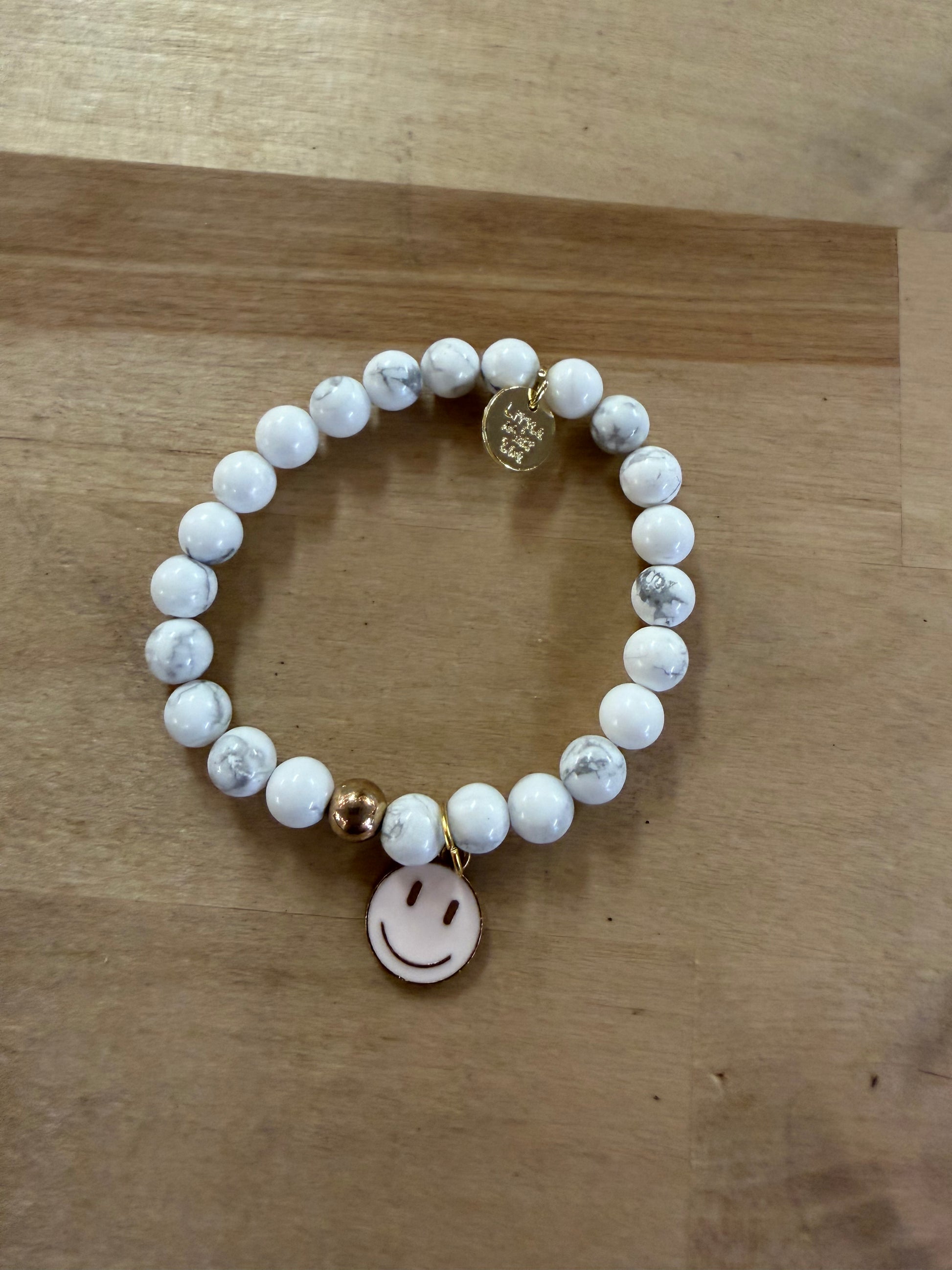 White marble beaded stretch bracelet with gold smiley face charm and logo tag